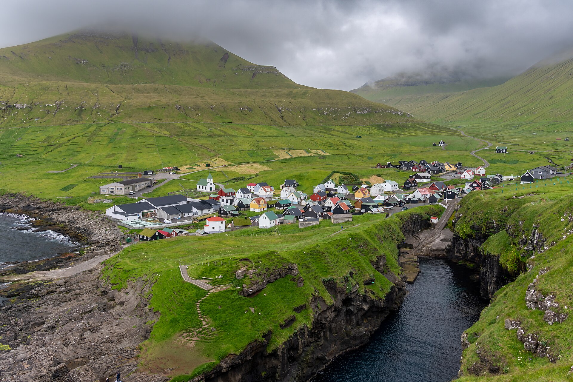 Gjógv auf den Färöern: farbige Häuser, grüne Landschaft und die zum Meer führende Schlucht